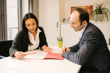 Zwei Personen sitzen im Rahmen eines Beratungsgesprächs an einem Tisch und schauen gemeinsam in eine Akte., © Stadt Köln, Kommunales Integrationszentrum