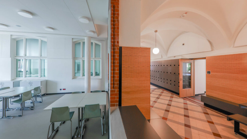 Wirkt wie eine Fotomontage, ist aber keine: links der neu eingefügte moderne Klassenraum in strahlendem Weiß mit dem rechts angrenzenden offenen Lernflur mit restaurierten Bodenfliesen und Gewölbedecken.