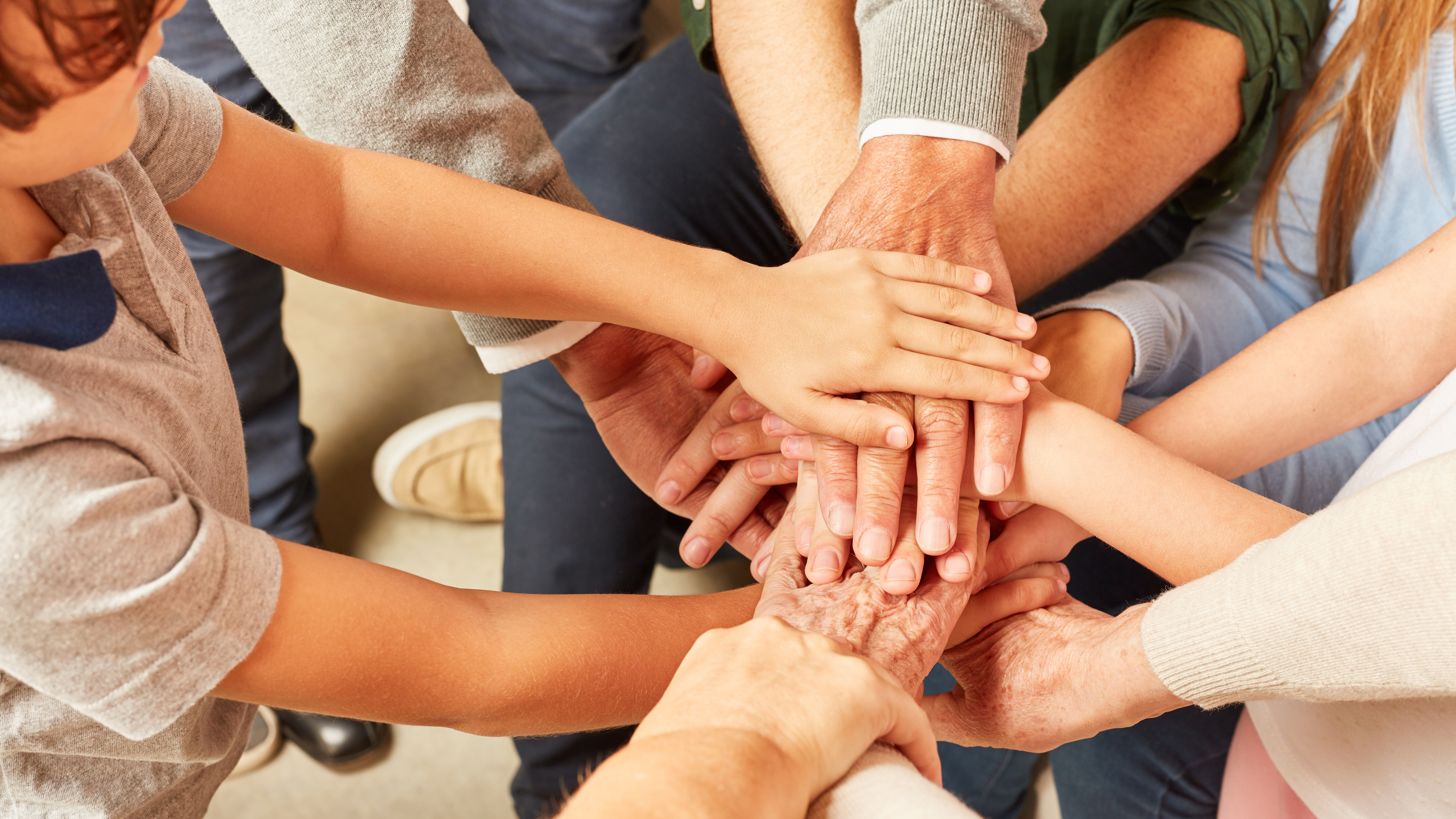 Eine diverse Menschengruppe hat die Hände im Kreis übereinander gelegt.
