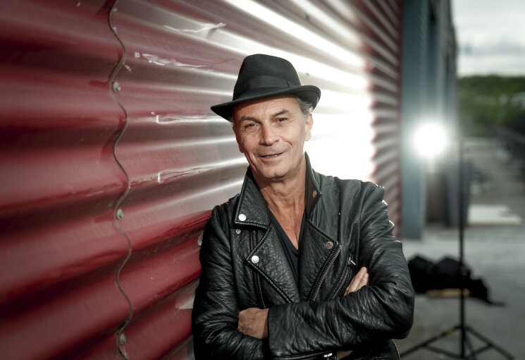 Das Foto zeigt den Ehrenamtspaten 2026 Peter Brings in schwarzer Lederjacke und mit schwarzem Hut, der sich an eine Mauer anlehnt. Im Hintergrund ist ein Scheinwerfer zu sehen, der Peter Brings von hinten anleuchtet., © Moritz Mumpi Künster