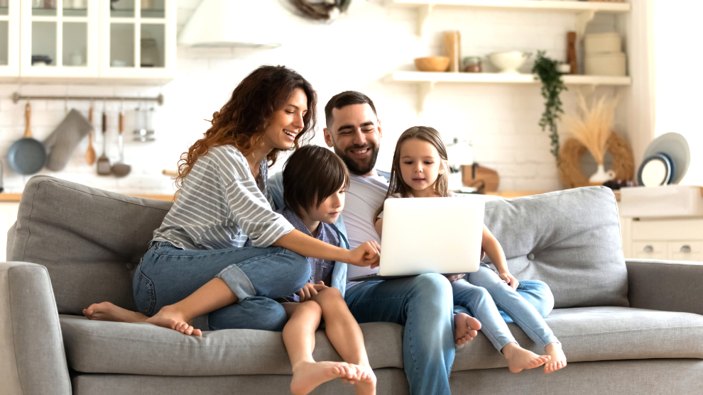 Vater, Mutter und zwei Kinder sitzen auf einer Couch und schauen